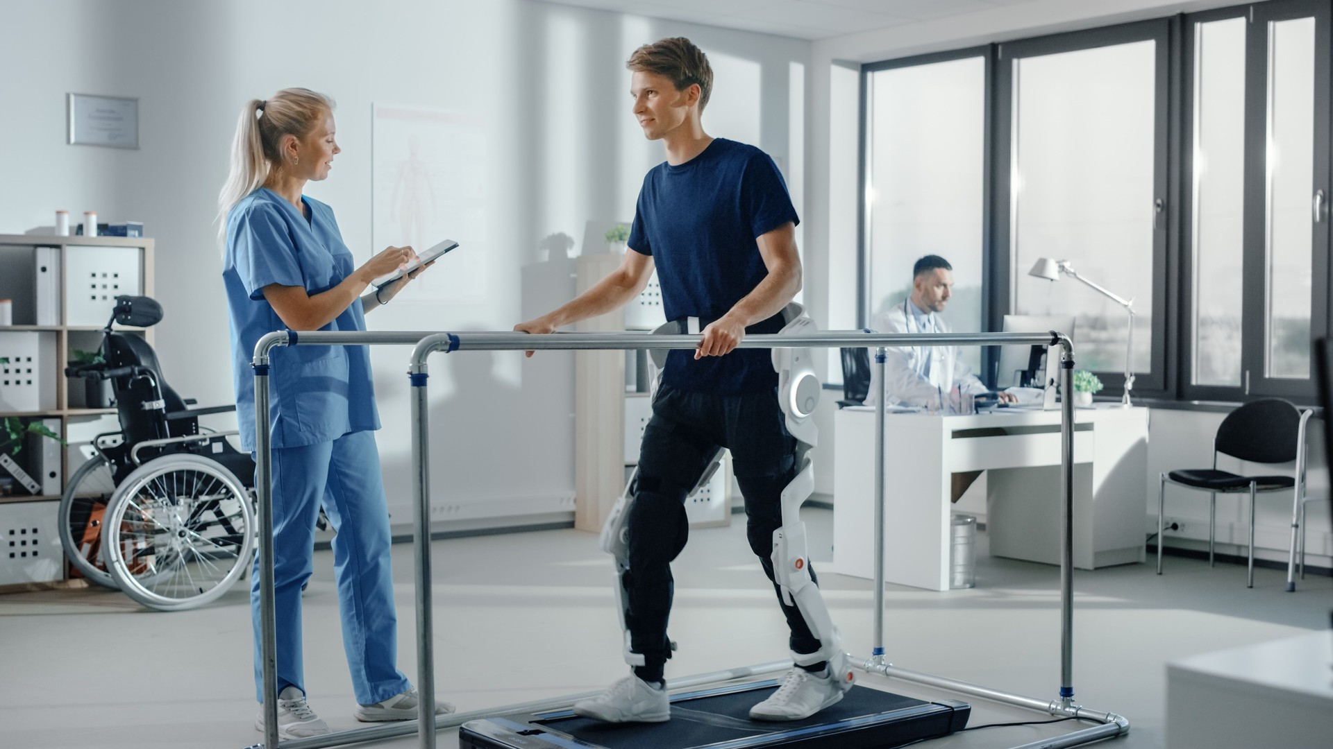 Modern Hospital Physical Therapy: Doctor Uses Tablet Computer, Helps Disabled Patient with Injury Walk on Treadmill Wearing Advanced Robotic Exoskeleton Legs. Physiotherapy Rehabilitation Technology